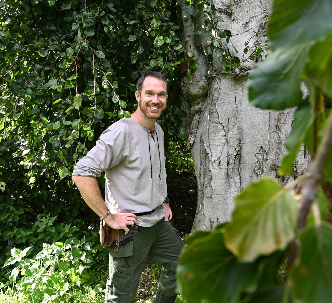 Max Schmidt lächelt in die Kamera am Fuße einer alten Buche.